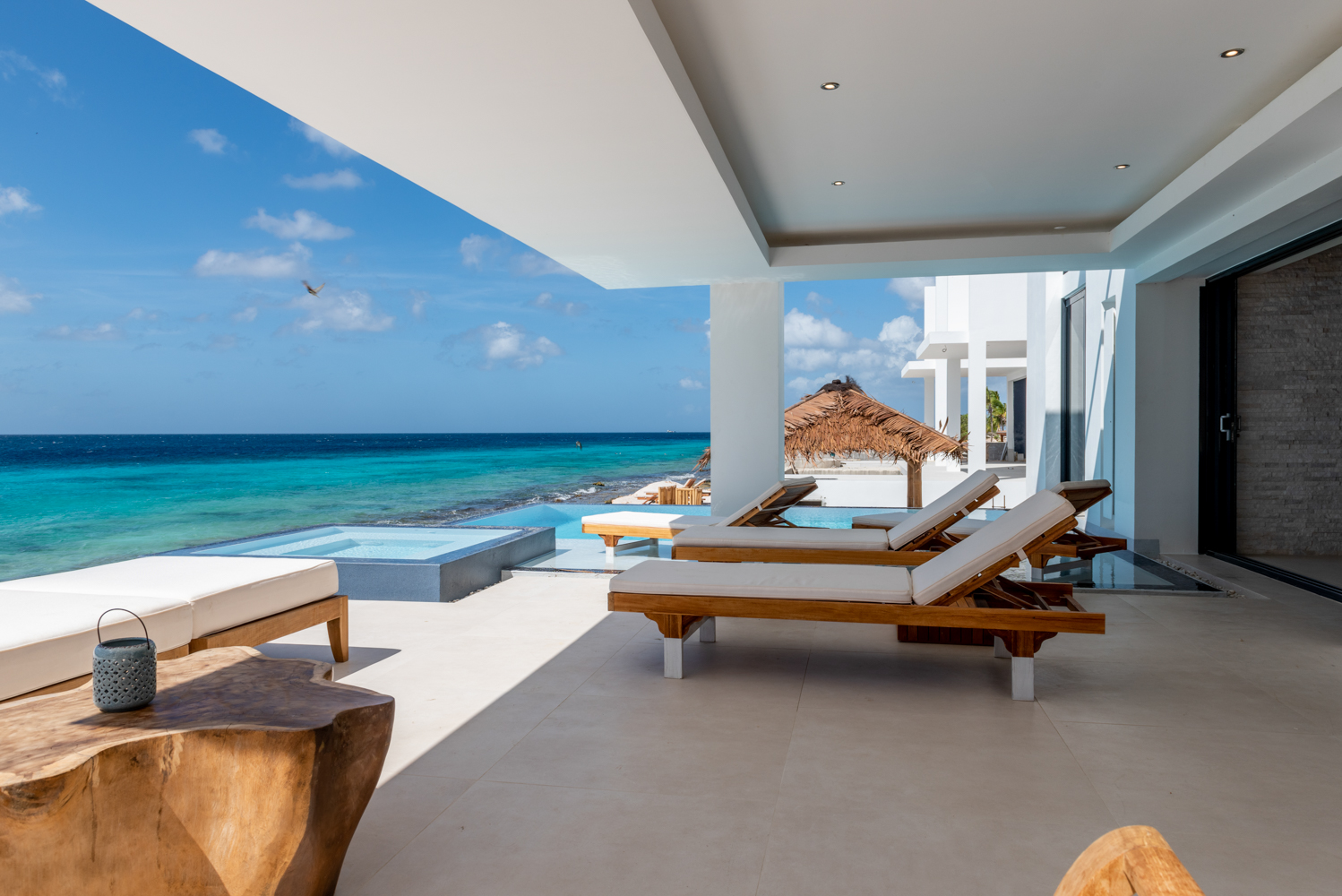 Luxury Bonaire villa with shaded oceanfront terrace, private plunge pool, teak loungers, and direct views of the turquoise Caribbean Sea.