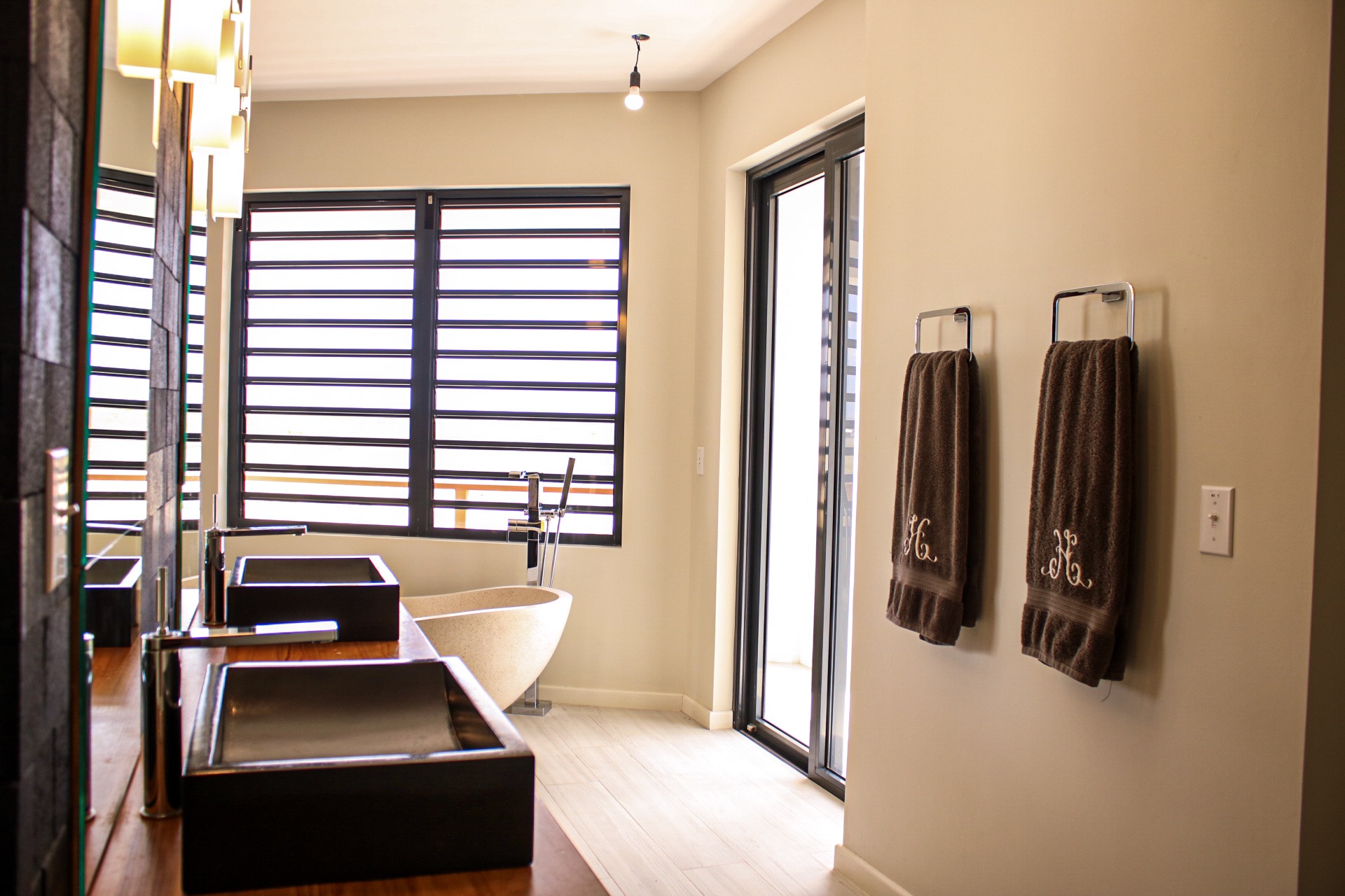 Luxury Bonaire villa spa bathroom with a freestanding stone soaking tub, double vanity with black vessel sinks on a wood countertop, and a private terrace door.