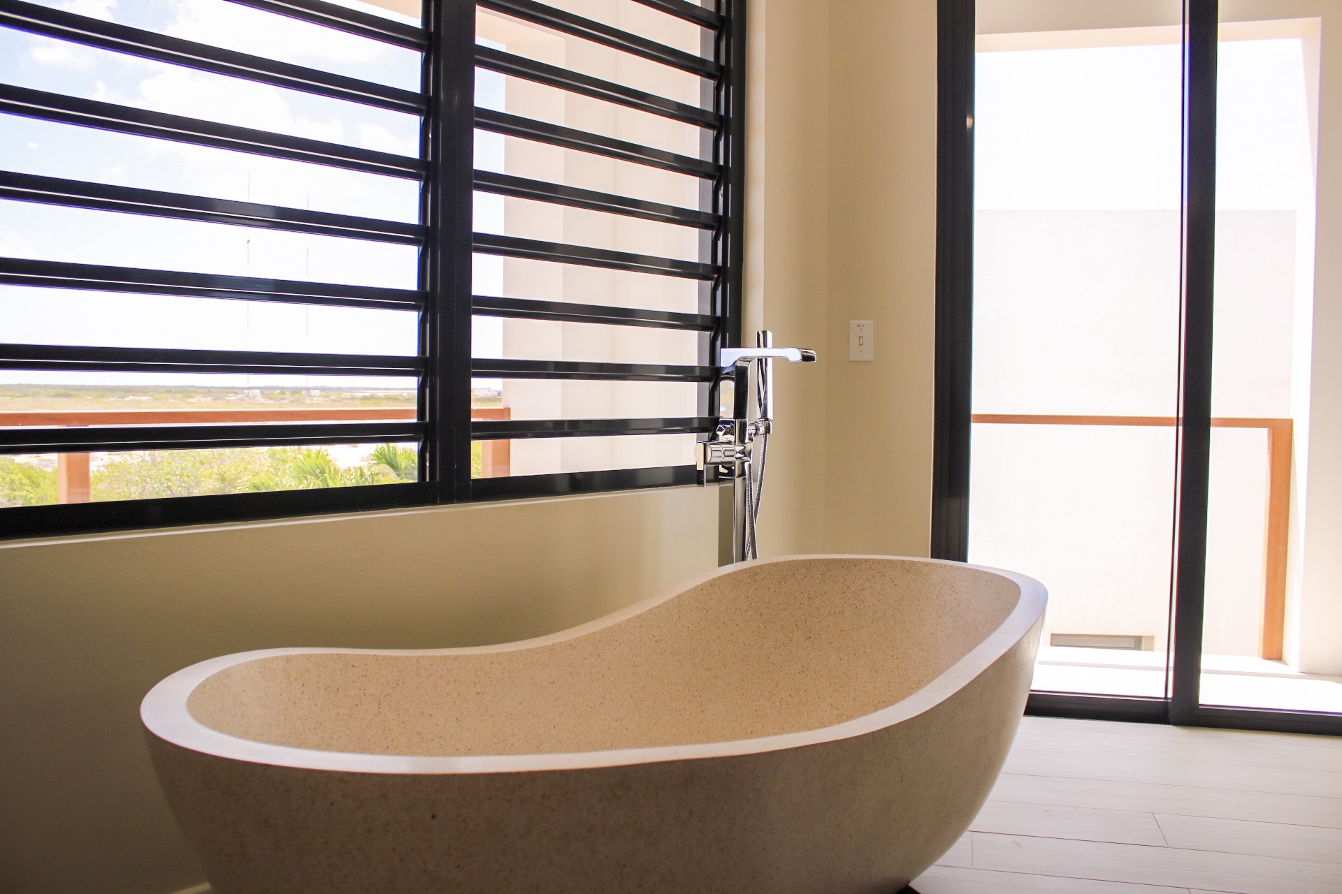 Luxury Bonaire villa spa bathroom with a freestanding stone soaking tub, modern chrome fixtures, and a large louvered window with views of the natural landscape.