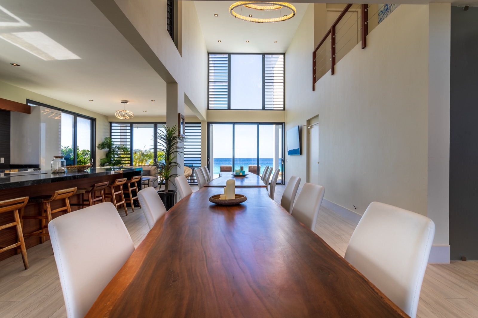 Luxury Bonaire villa dining room with double-height ceiling, live-edge wood table, and floor-to-ceiling windows with panoramic ocean view.