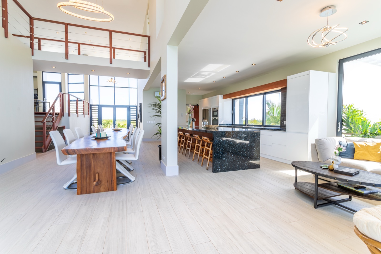 Luxury Bonaire villa interior with open-plan living, featuring a double-height dining room, live-edge wood table, and gourmet kitchen with a black granite island.