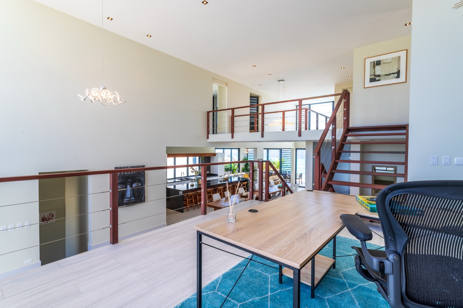 Mezzanine view of a luxury Bonaire villa with double-height ceilings, a modern floating wood staircase, and an open-plan gourmet kitchen with ocean views.