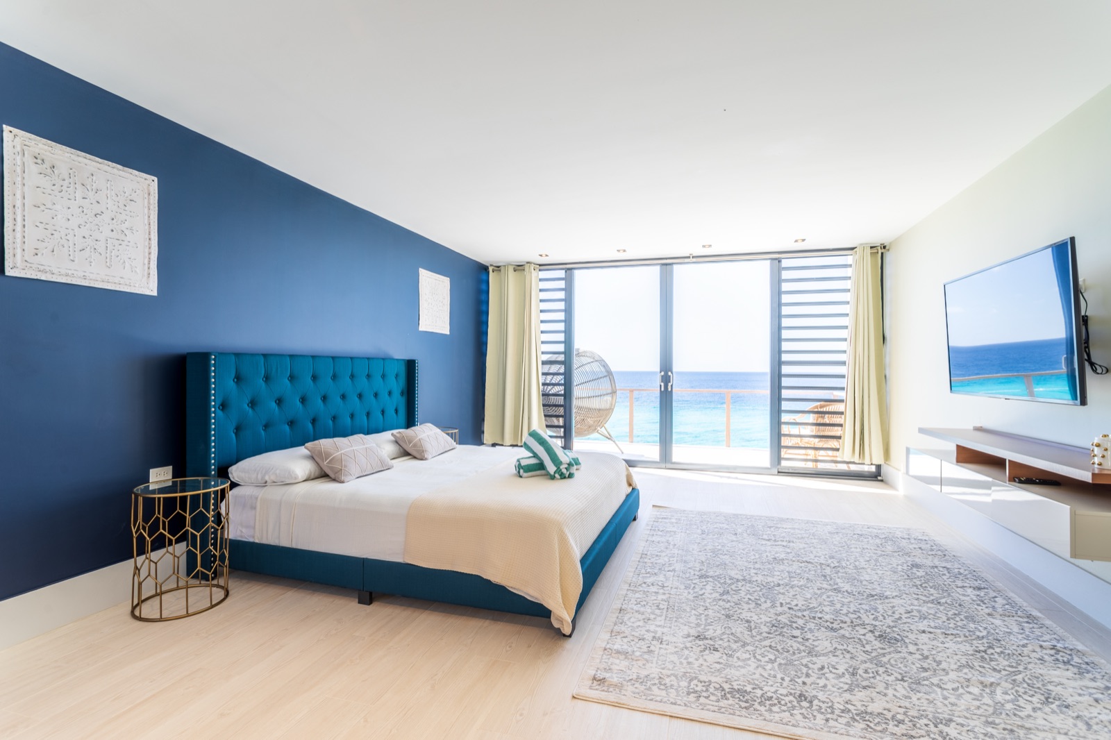 Luxury Bonaire villa master suite with a blue tufted king bed and floor-to-ceiling glass doors opening to a private balcony with panoramic ocean views.