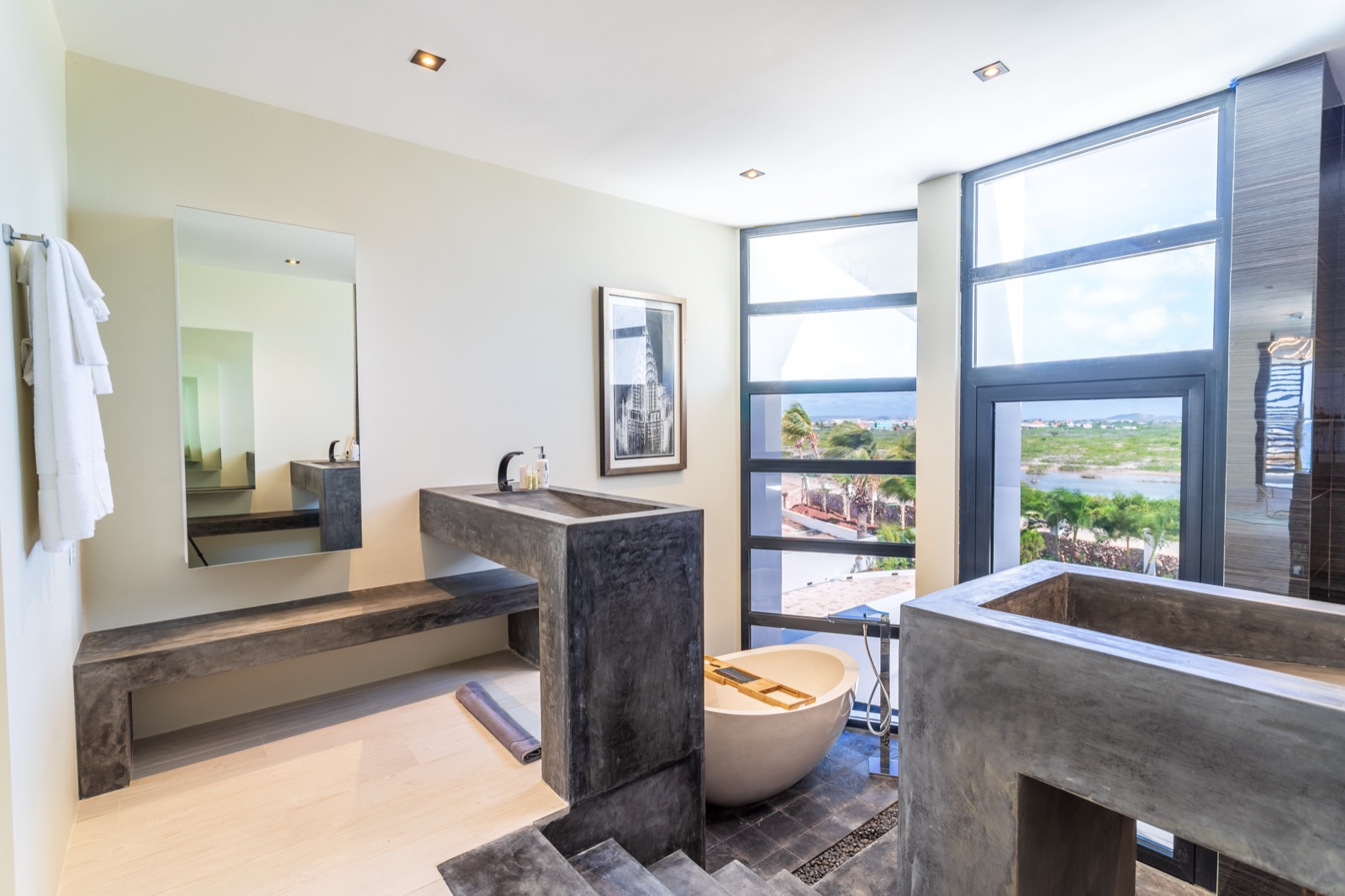 Luxury Bonaire villa spa bathroom with polished concrete vanities, a freestanding soaking tub, and floor-to-ceiling windows overlooking the lagoon and ocean.