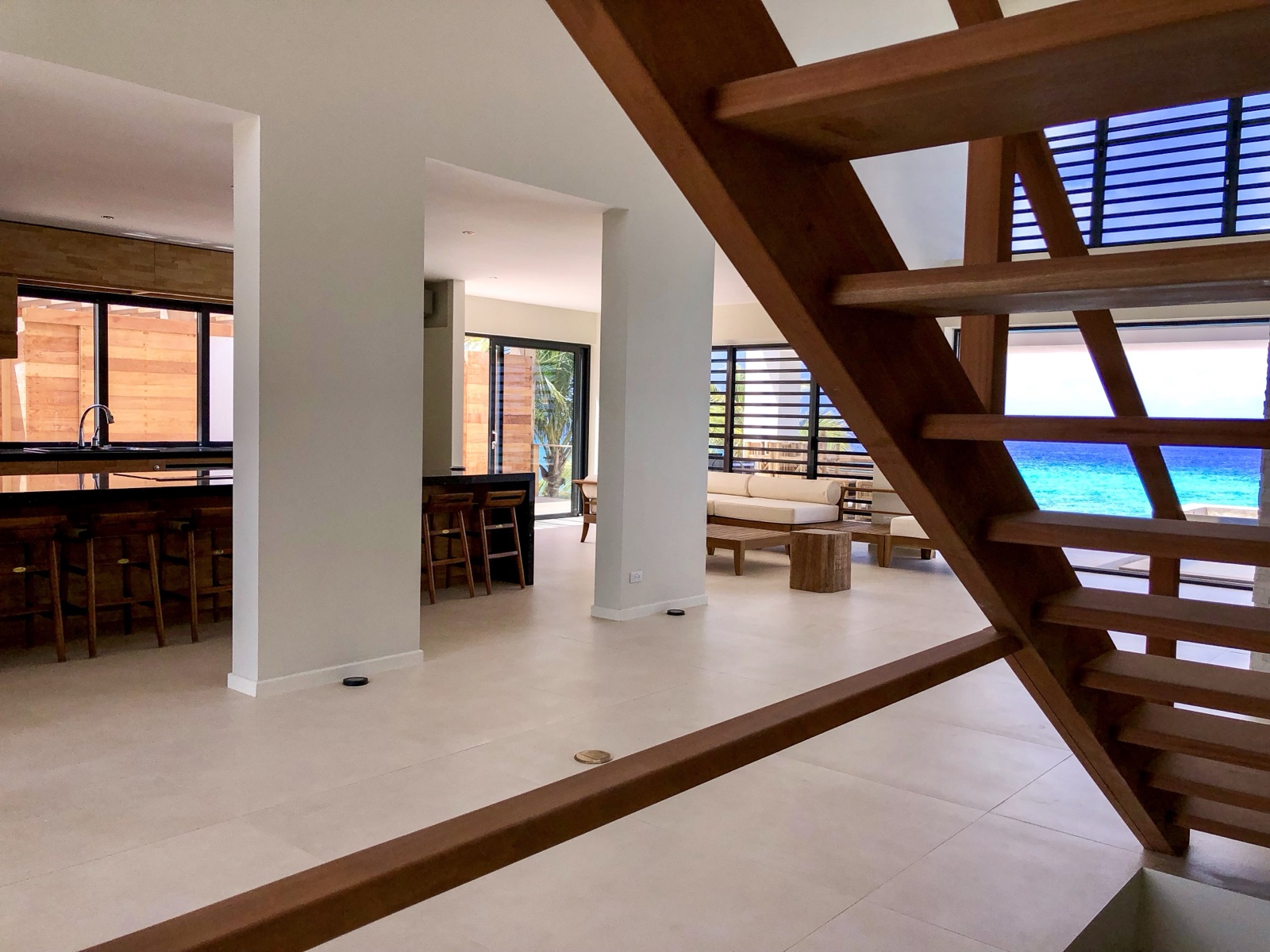 Luxury Bonaire villa interior with an open-plan living room, modern wooden staircase, and a direct view of the turquoise Caribbean ocean.